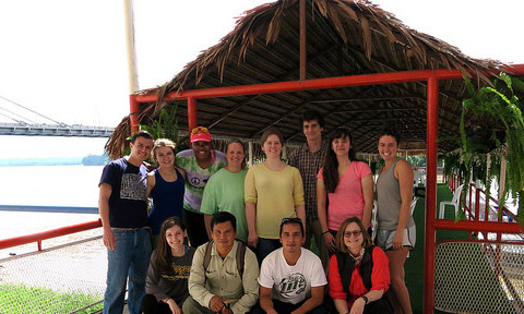 The Ecuador study abroad travelers pose under a palm thatch roof following a trip up the Napo River.